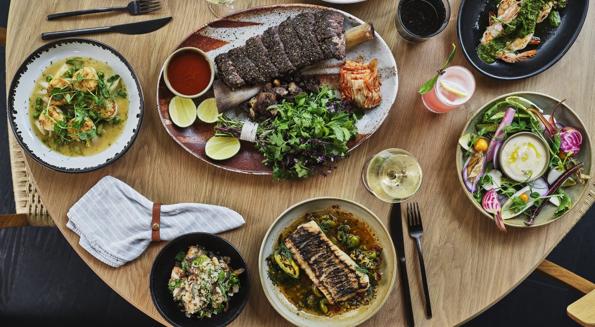 A bird's eye view of a dinner table at Stanly Ranch, with a large rib dish, glasses of wine, cocktails, and other elaborate dishes.